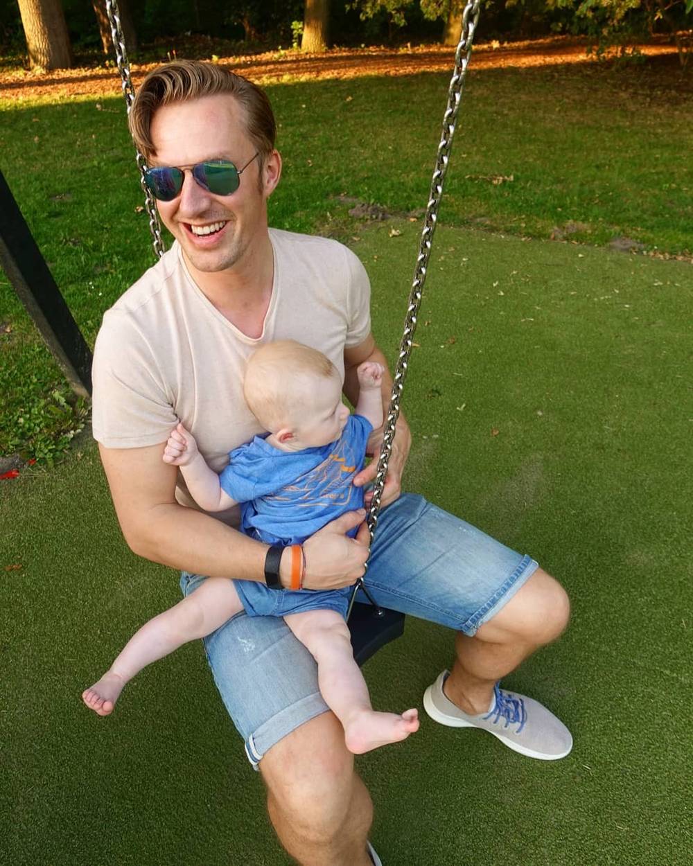 A man laughs while sitting on a swing in a park at dusk.