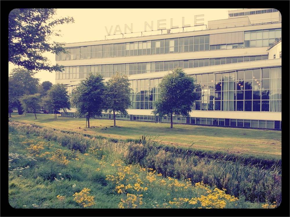 The Van Nelle Fabriek's modernist glass facade rises above a grassy field.