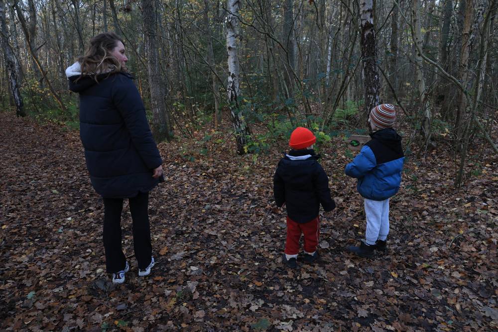 A woman and two children stand together in an autumn forest.