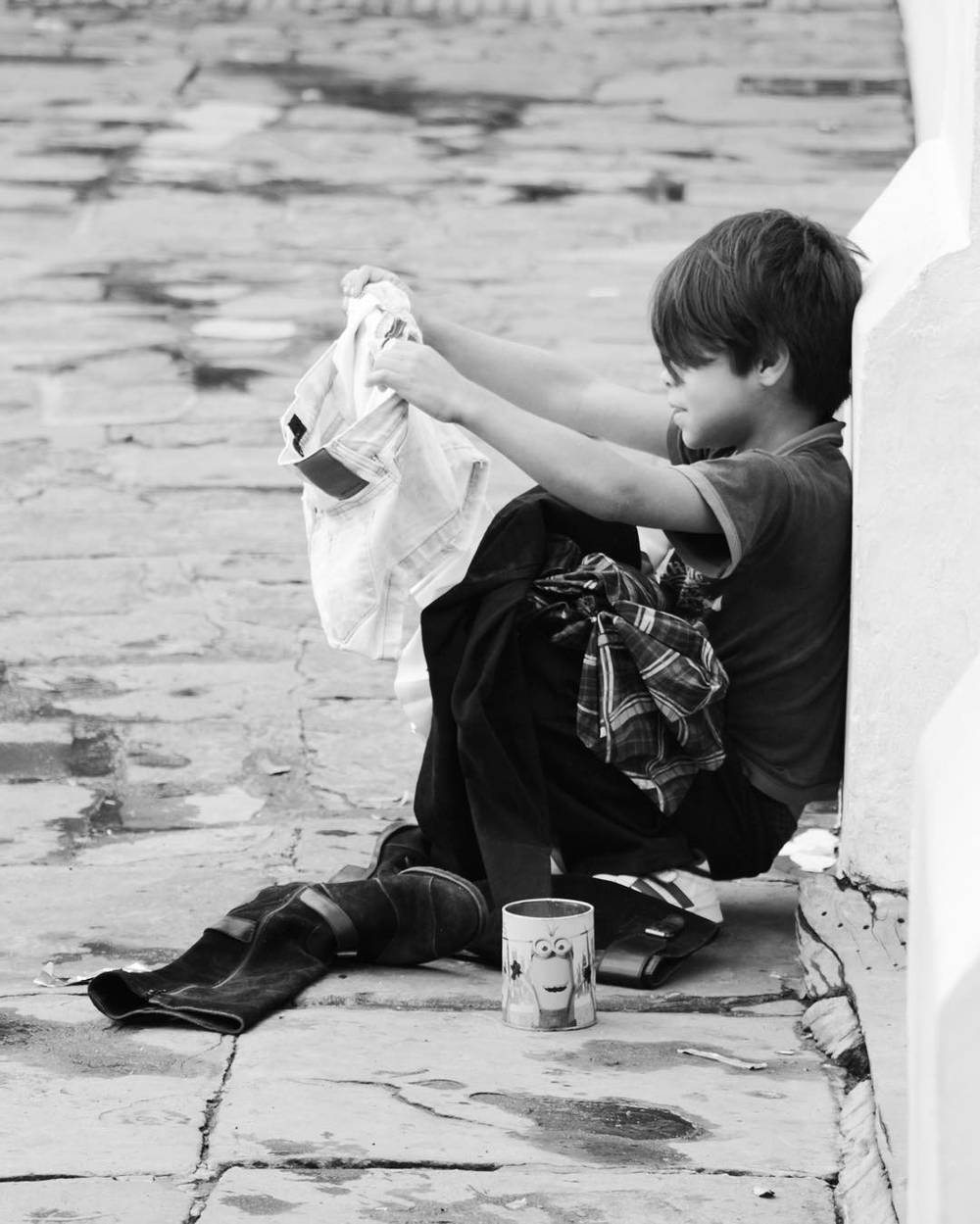 A black and white photo of a child sitting against a wall, drying their hands with a cloth.