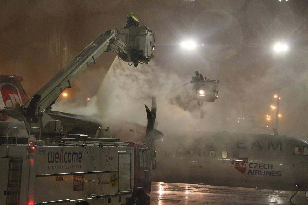 A de-icing truck spraying a Czech Airlines plane on a snowy airport tarmac at night.
