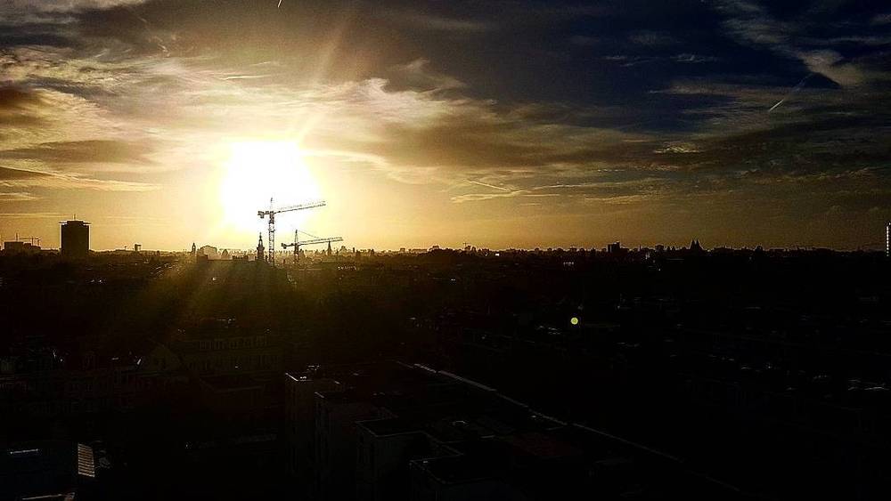 A city skyline with construction cranes silhouetted against a glowing sunset.