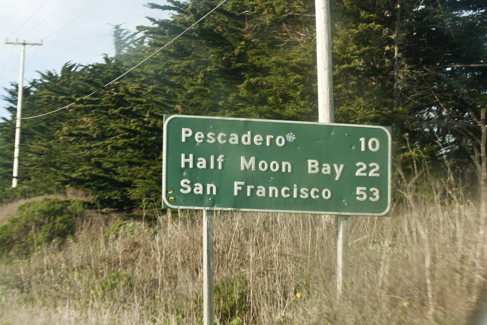 A green highway sign lists distances to Pescadero, Half Moon Bay and San Francisco.