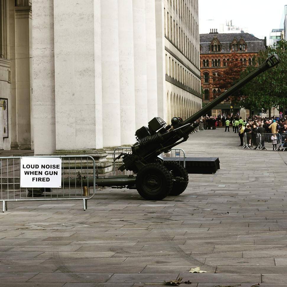 A historic cannon displayed outside a columned building, with a sign warning of loud noise when fired.