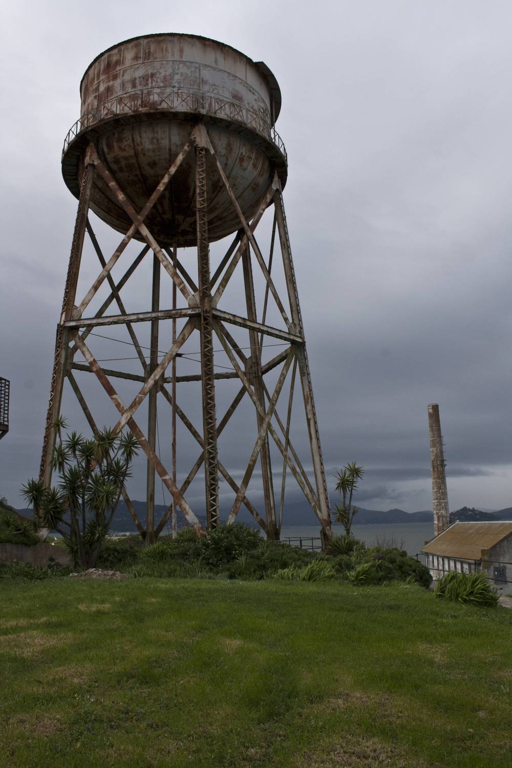 A rusted wooden water tower stands on a grassy patch at Alcatraz.