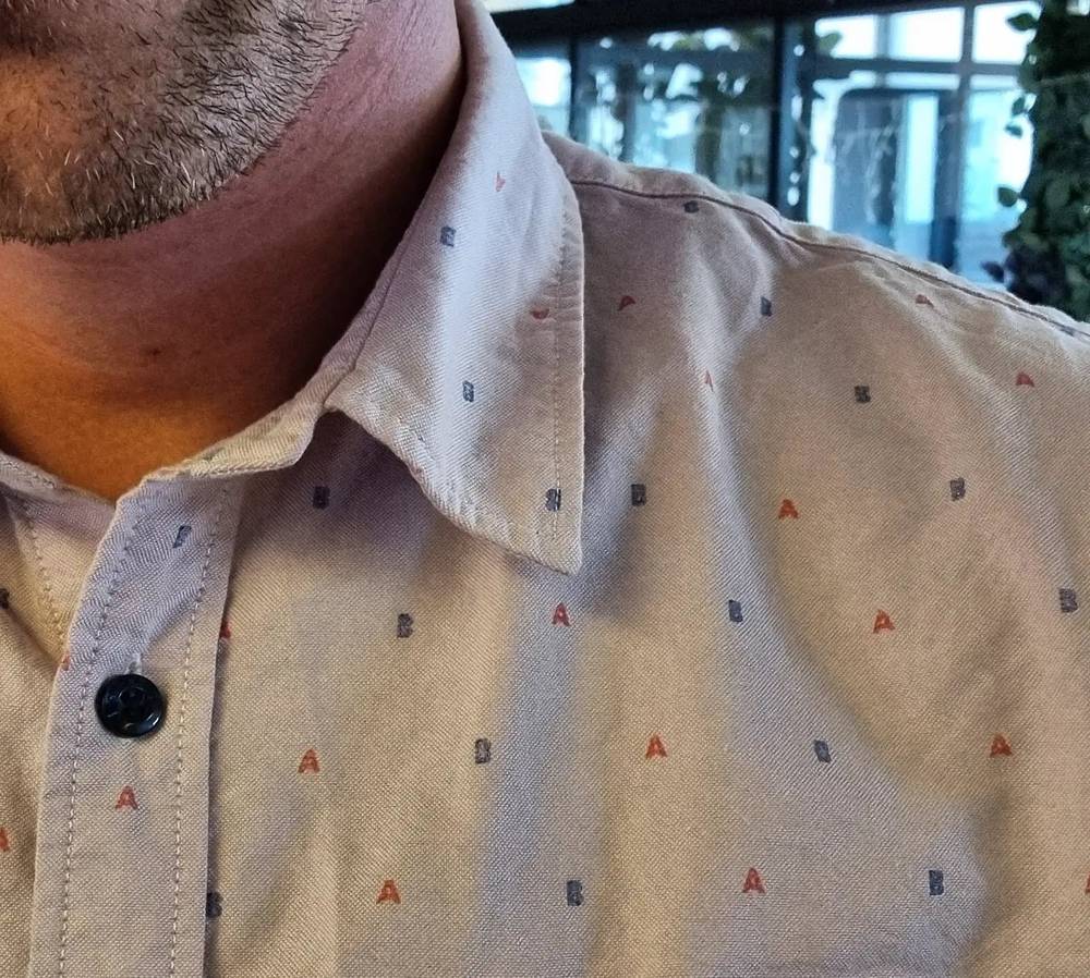 Close-up of a patterned shirt collar covered in small embroidered letter icons.