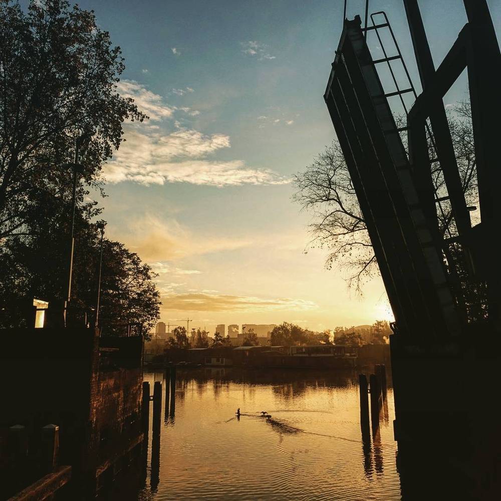 A drawbridge silhouetted against a sunset with rowers on the water below.
