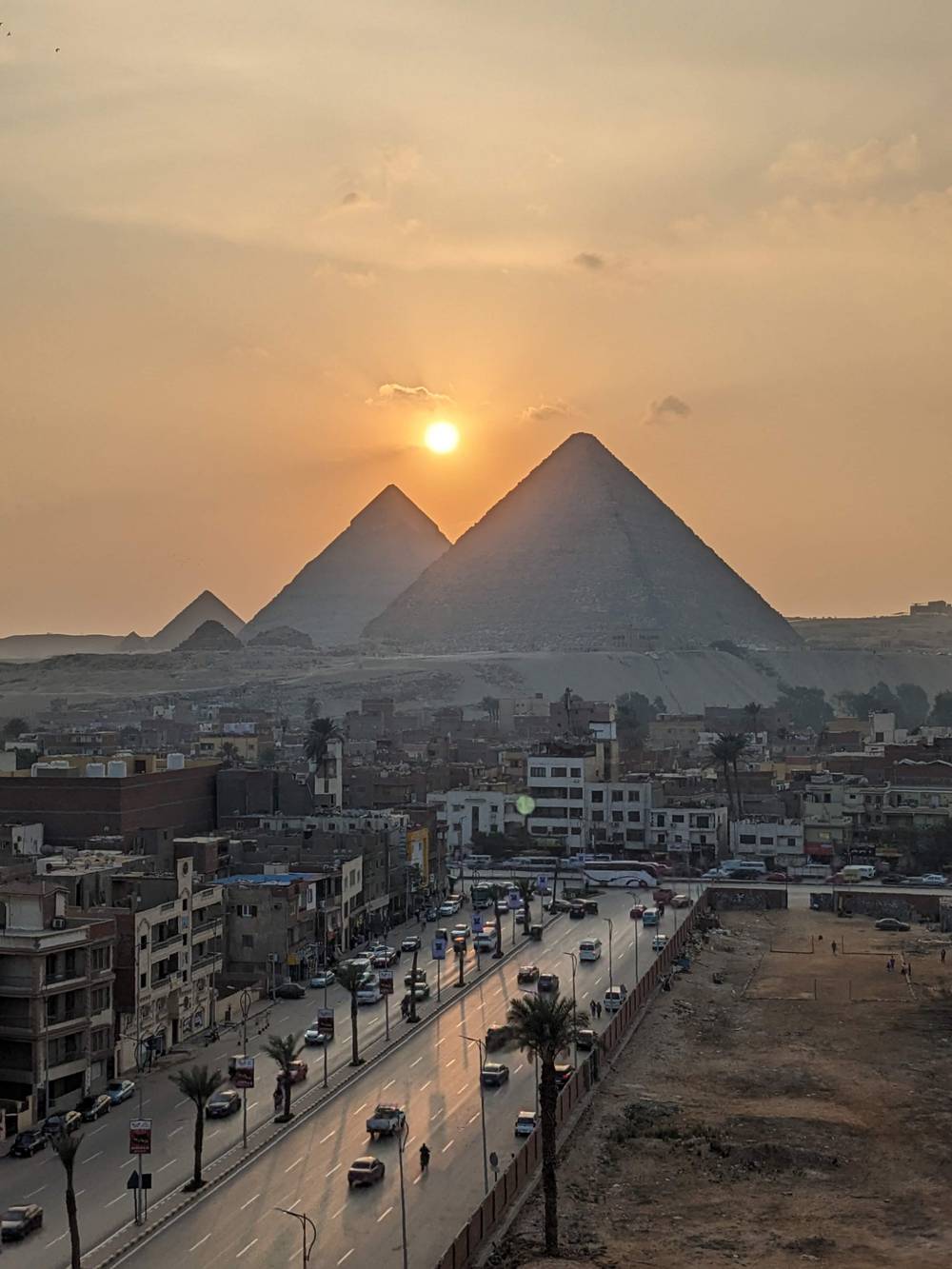 The three pyramids of Giza seen above an urban area at sunset