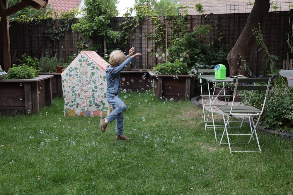 4yo boy dancing on the garden on a grass in a cloud of soap bubbles