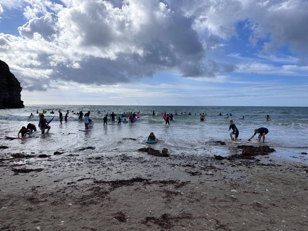 Lots of people on bodyboards in the shallow waters of a beach.