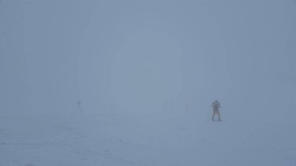 A lone skier barely visible on a snowy slope engulfed in thick fog.