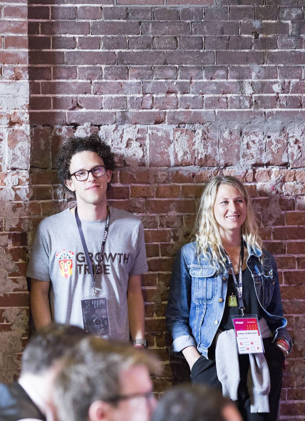 Two attendees, one in a Growth Tribe t-shirt, stand against a brick wall.