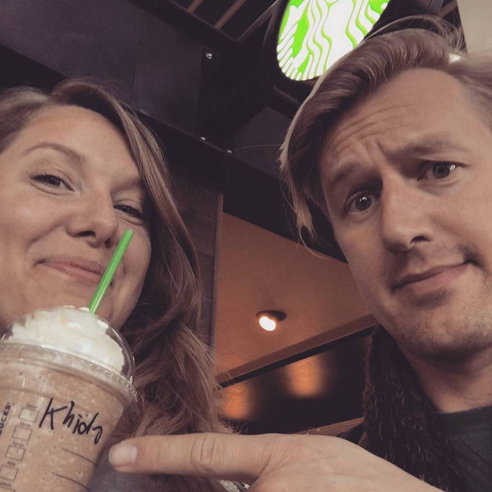 Two people smiling for a selfie while holding iced coffee drinks in a café.