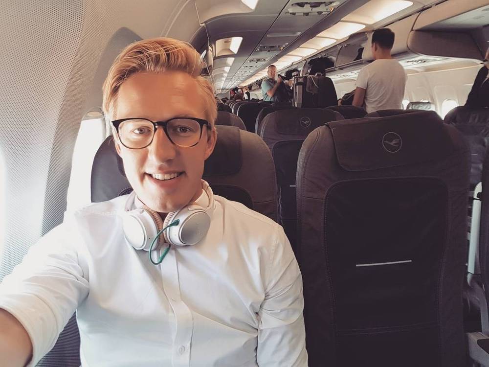 Selfie of a man wearing headphones seated on an airplane.