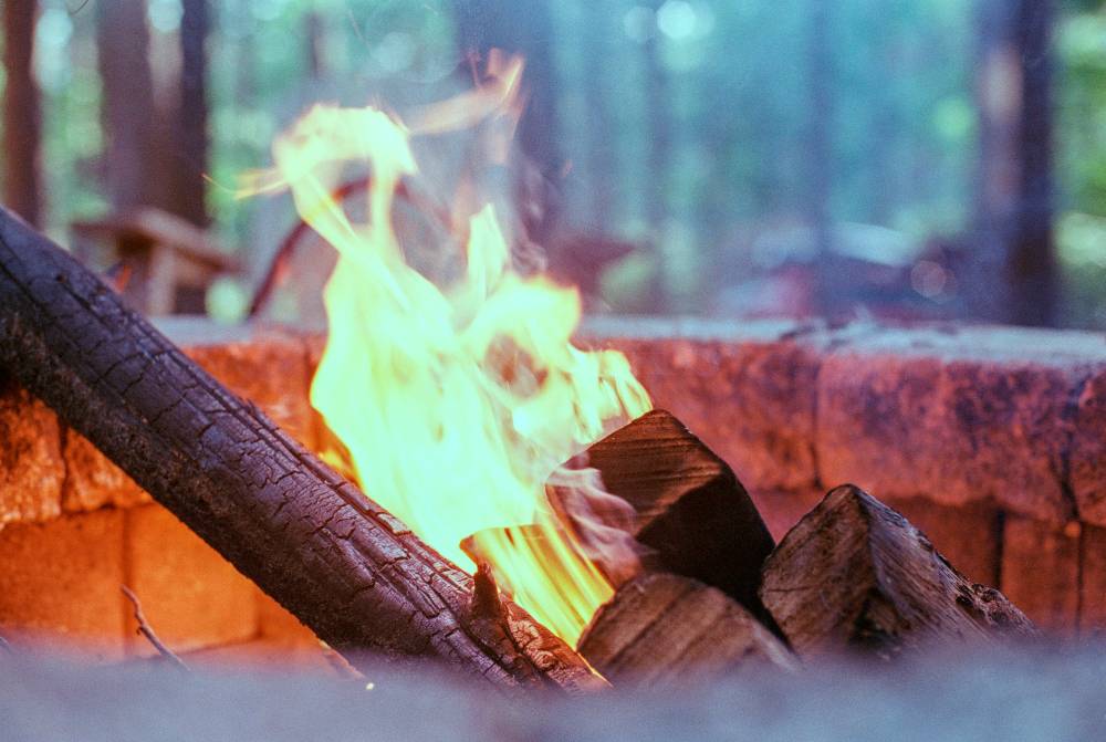 A campfire with bright yellow flames dancing over charred logs inside a stone fire pit.