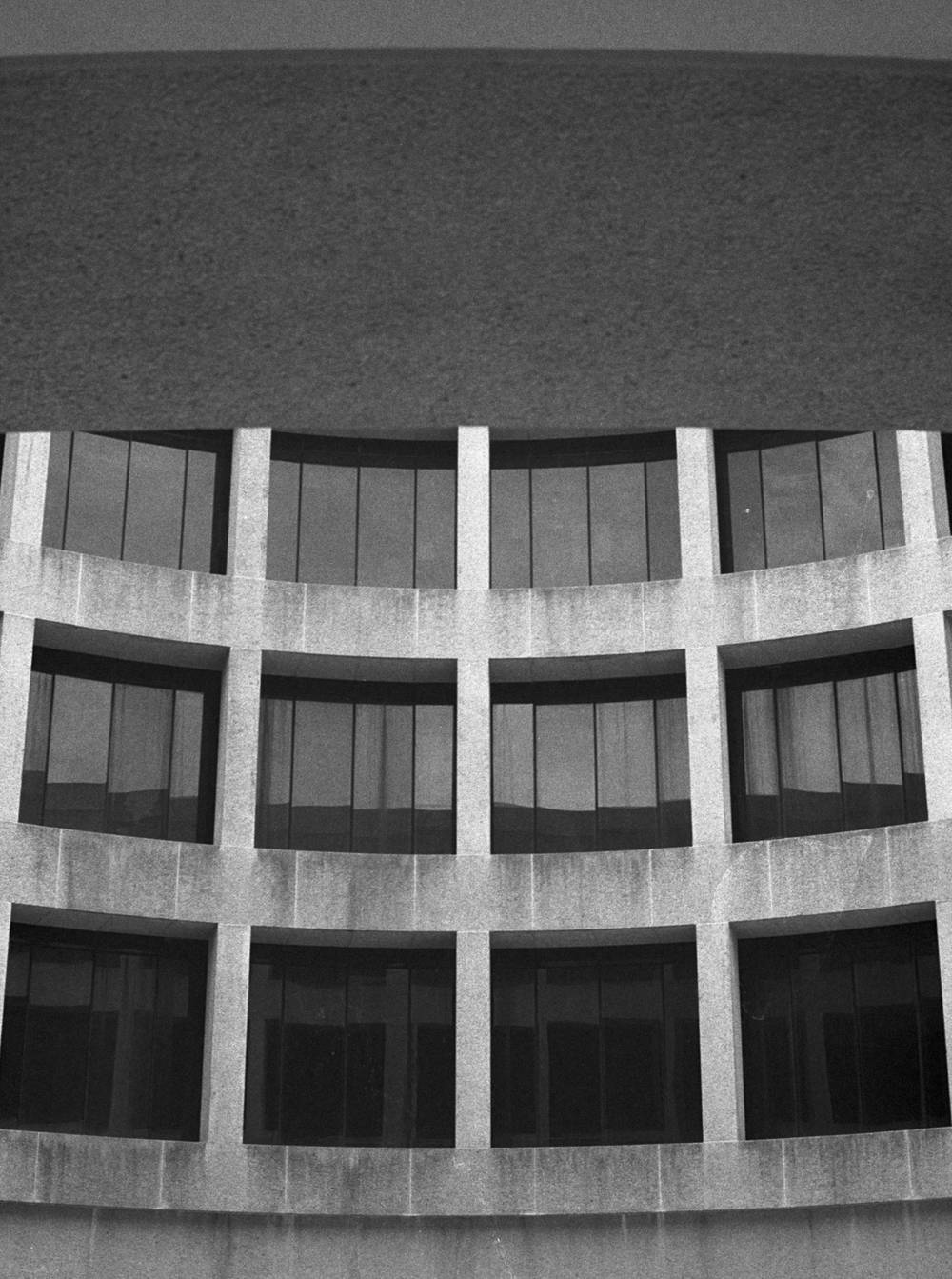 A curved building facade features a grid of dark, recessed windows framed by light-colored stone.