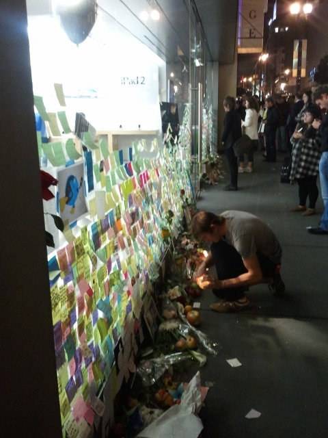 A wall covered in colorful sticky notes serves as a makeshift memorial outside an Apple store.