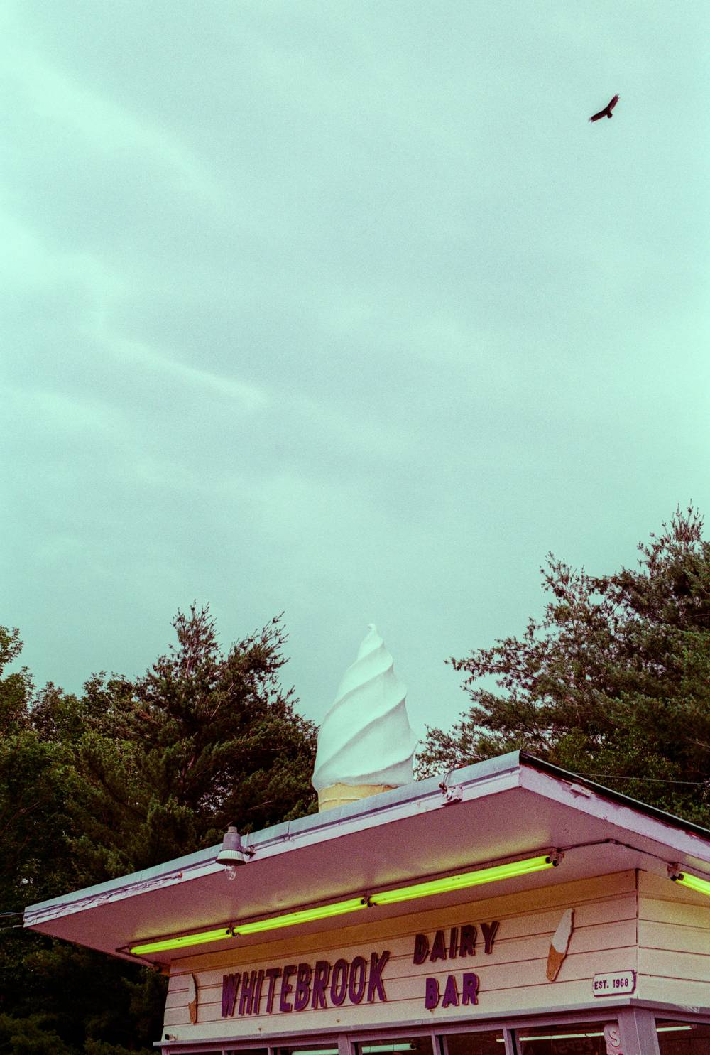 Whitebrook Dairy Bar with a giant soft-serve ice cream cone on its roof under a pale sky with a flying bird.