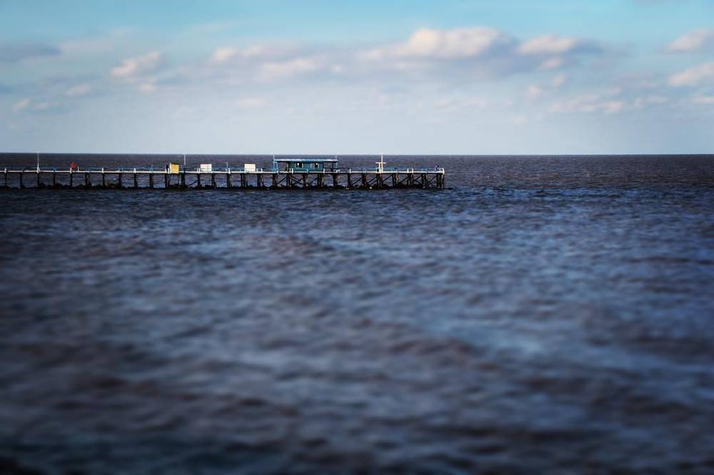 A pier extending into calm dark blue sea water under a clear sky.