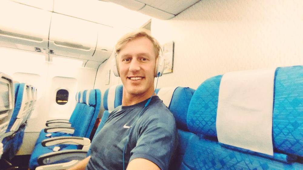 A man takes a selfie wearing headphones in an airplane seat.