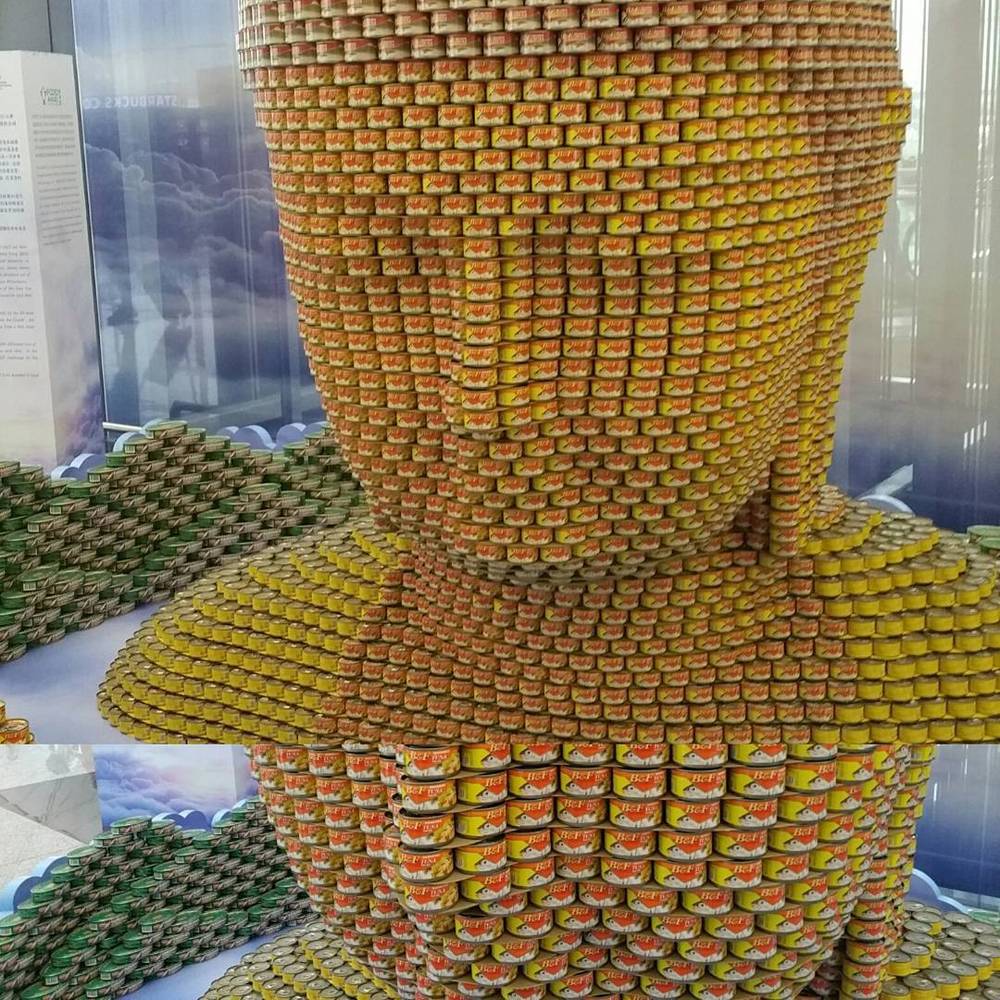A large sculpture made entirely of stacked tin cans, shaped like a robed figure.