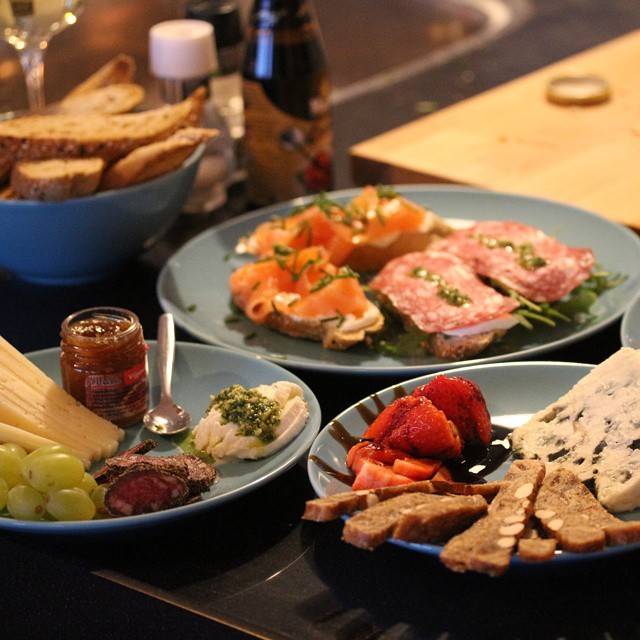 A spread of appetizer plates including cured meats, cheeses, bread and fruit on a table.