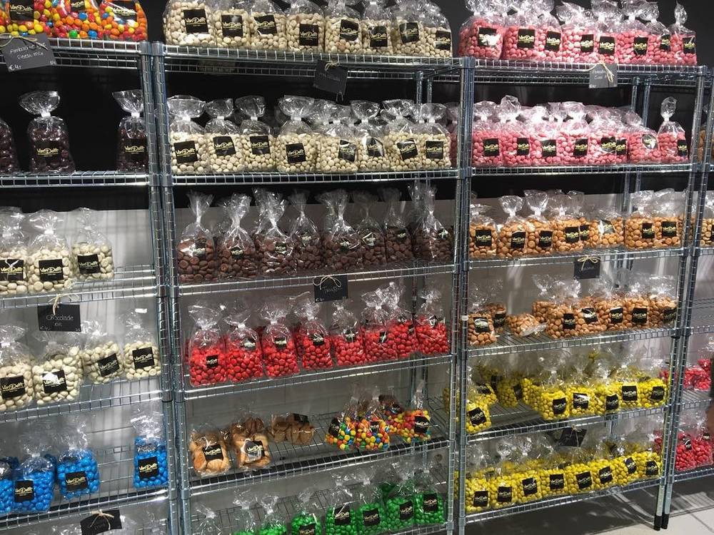 Shelves of bagged candy and nuts for sale, sorted by color and type.