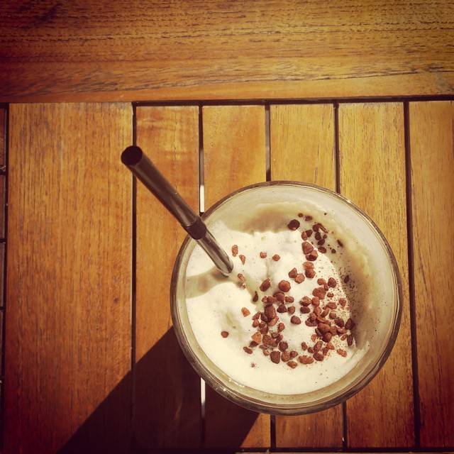 A glass of beer topped with foam and cocoa-dusted nuts on a wooden table.