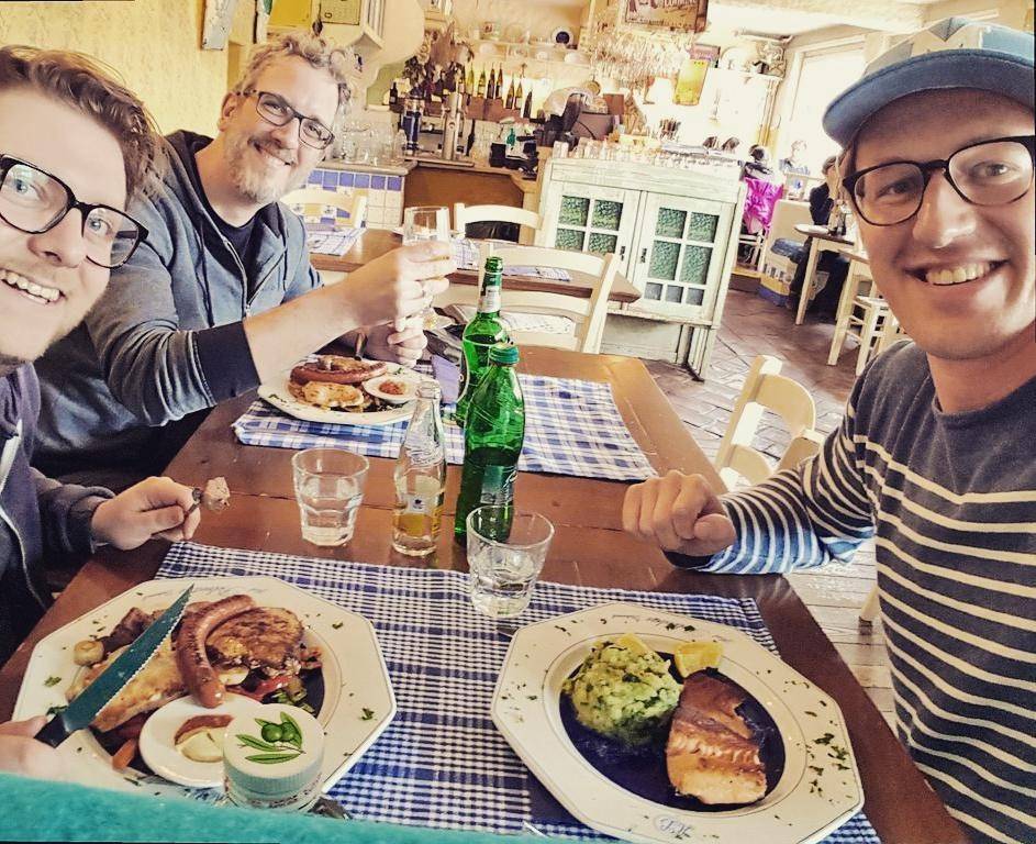 Group of friends toasting drinks at an outdoor restaurant table with plates of food.