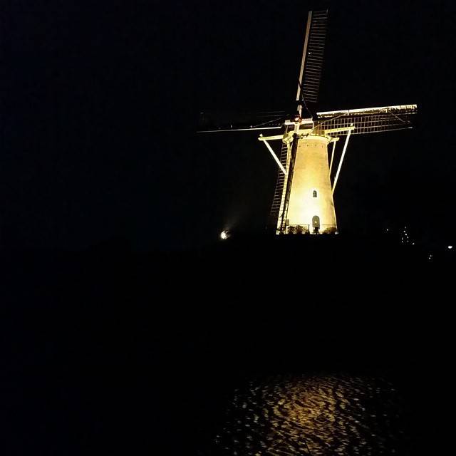 A traditional Dutch windmill lit up at night, reflected in the water.