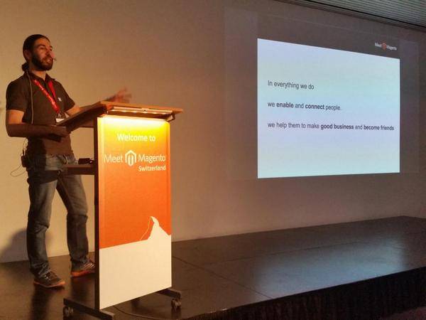 A man speaks at a lectern in front of a slide about enabling and connecting people, at Meet Magento Switzerland.