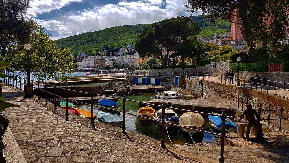 A small stone harbour with rowing boats moored along a waterfront promenade.
