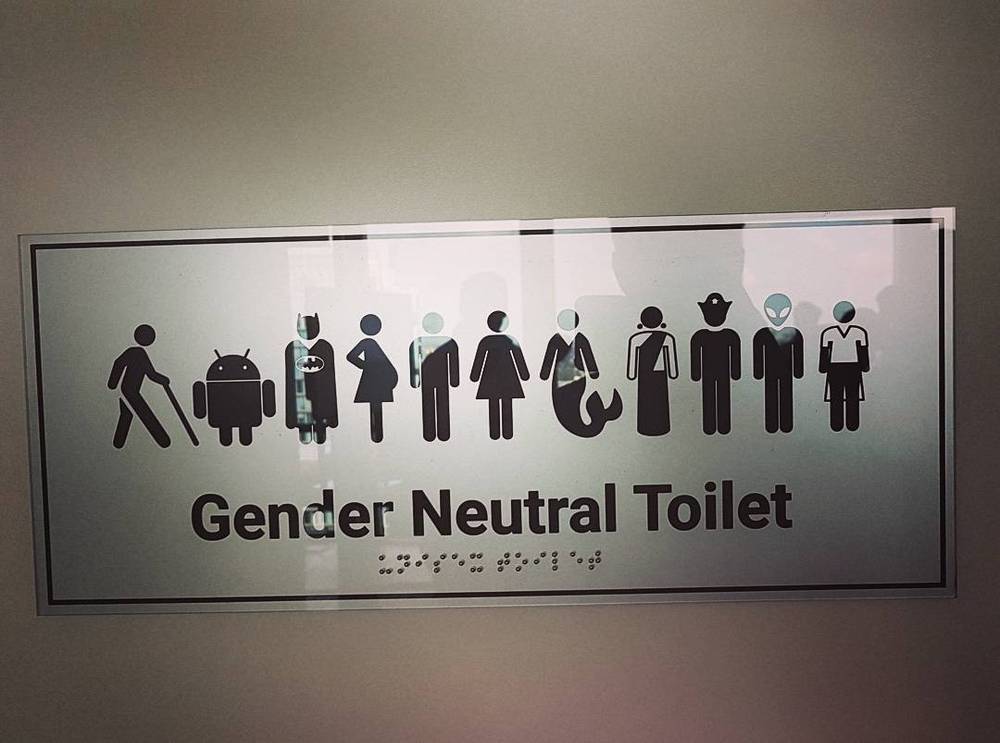 A wall sign reading "Gender Neutral Toilet" above a row of pictograms including a robot and an alien figure.