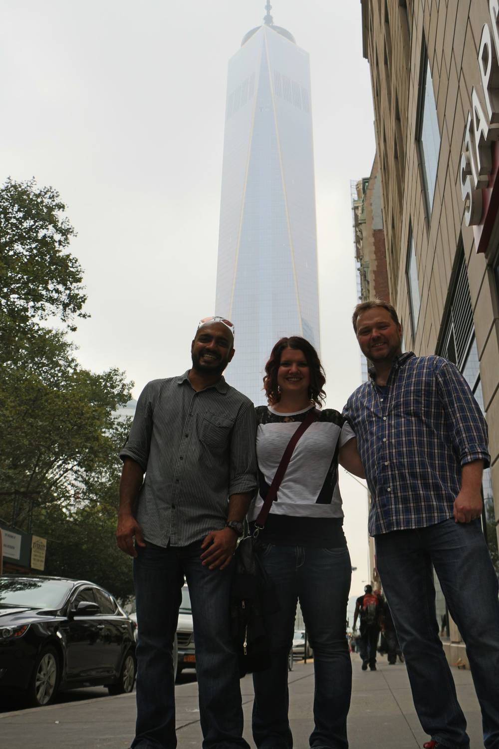 Three friends pose together on a street beneath One World Trade Center.
