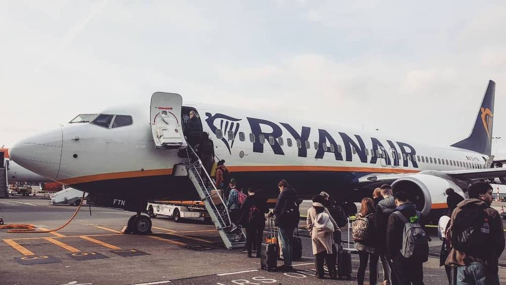 Passengers board a Ryanair plane via steps on an airport tarmac.