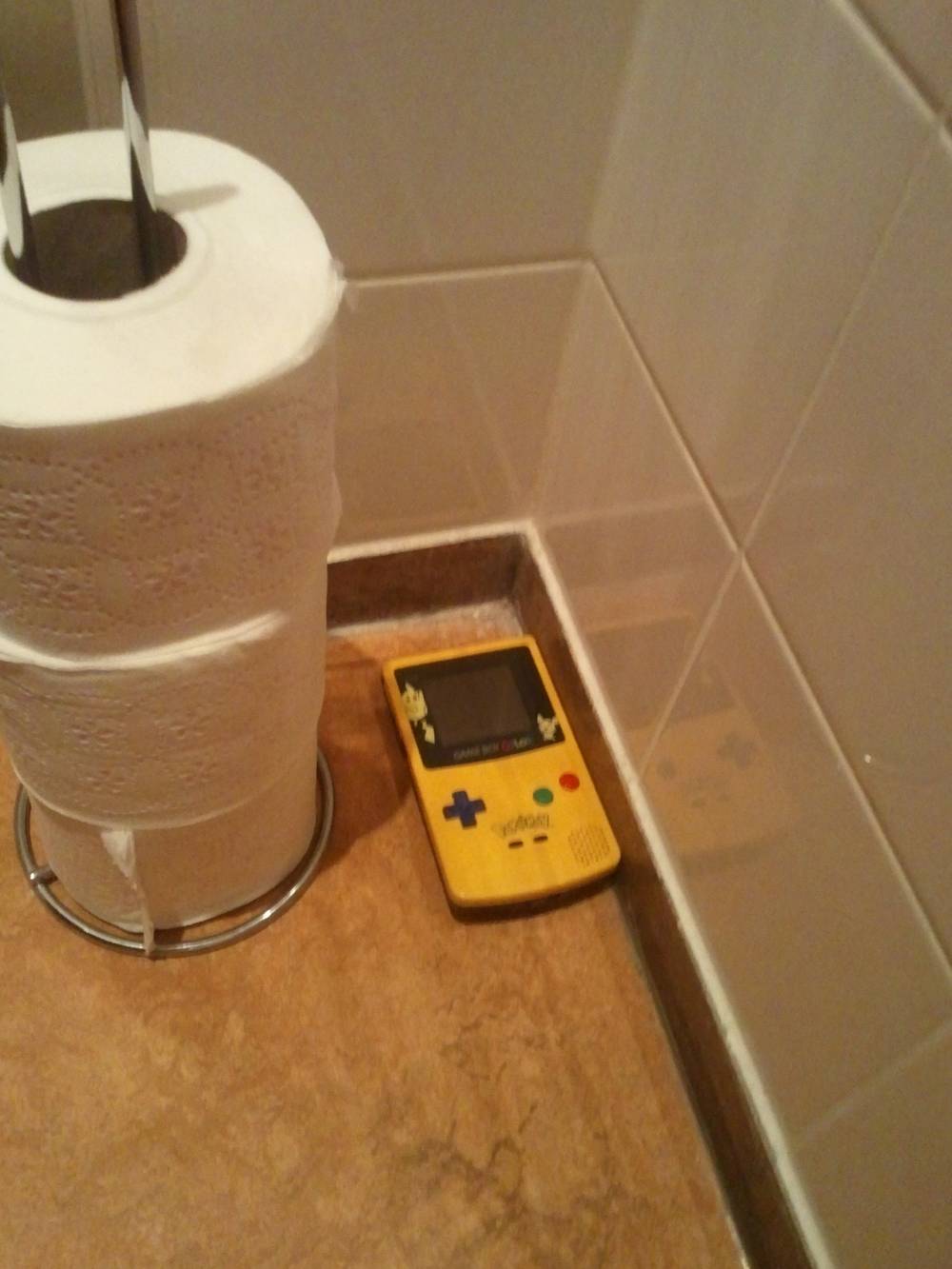 A Game Boy console is playfully balanced on a toilet paper holder at the office.