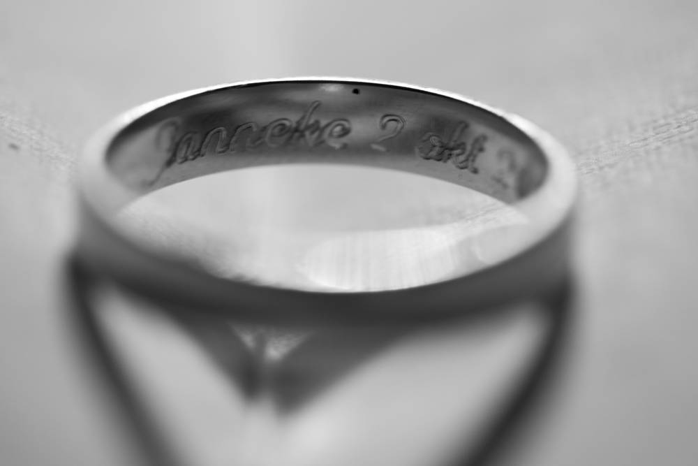 A black-and-white macro shot of a wedding ring engraved with a name and date on the inside.