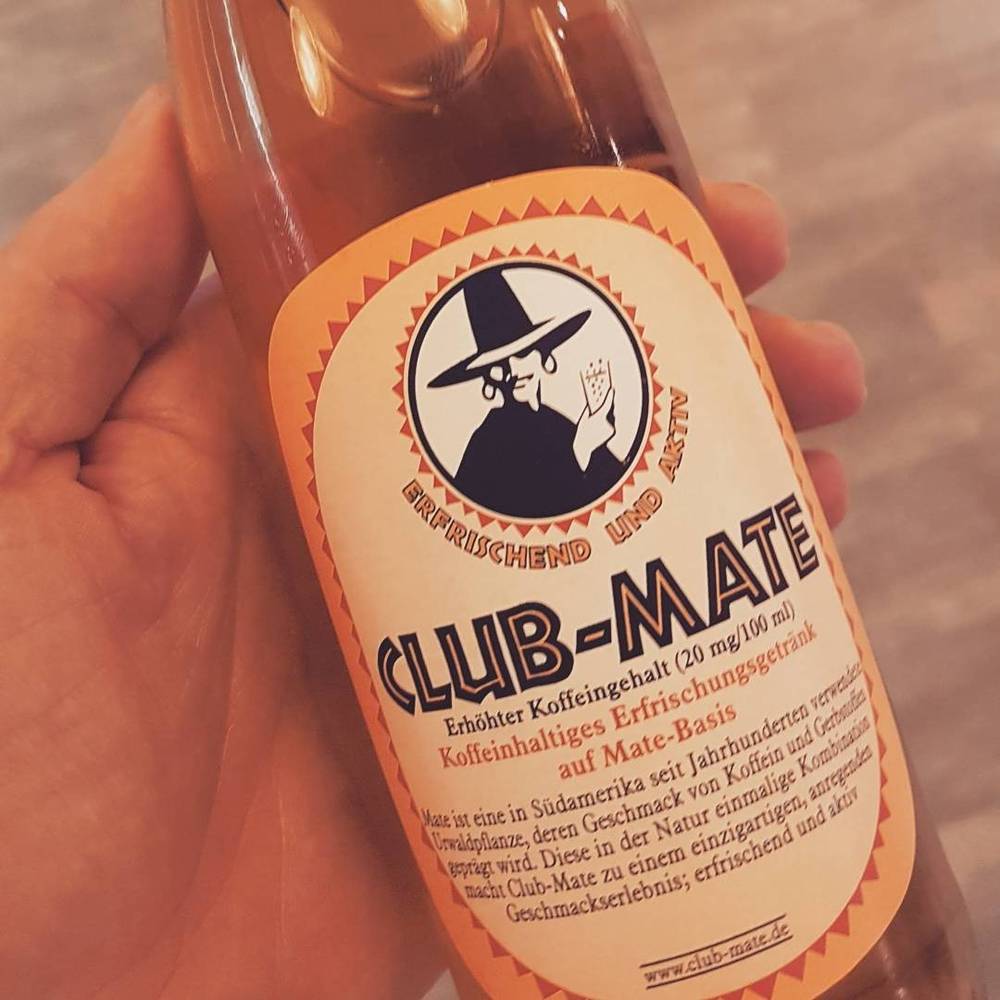 A hand holding a bottle of Club-Mate, a German caffeinated soft drink.