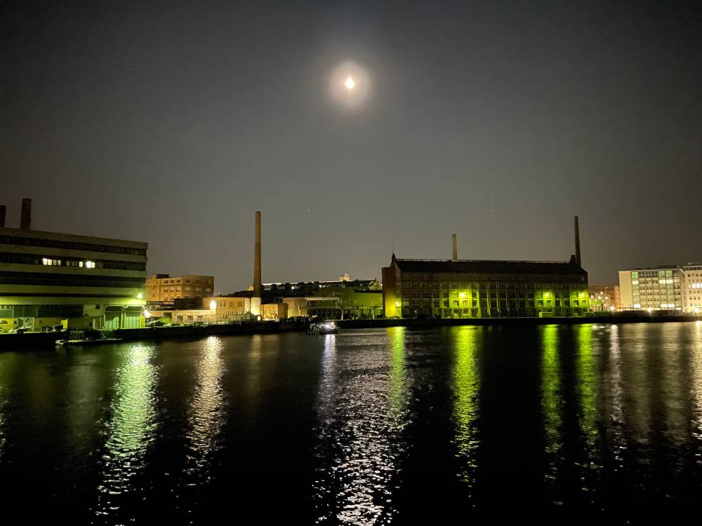 The moon over a view of industrial buildings and the river Spree