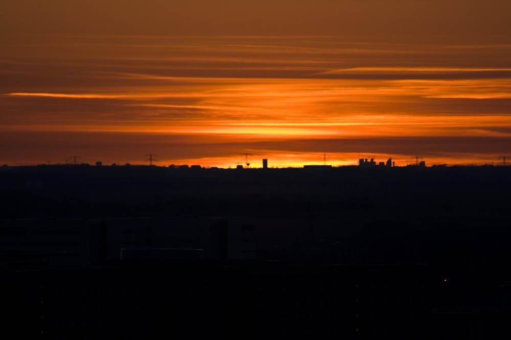 A fiery orange sunset glows over a city skyline.