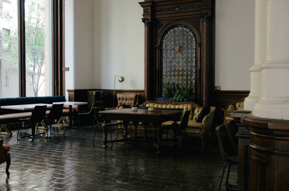 interior shot of an older building, tables and chairs placed around the room, with a fancy as fuck velvet couch in the background obscured partially by a table. the window lighting up the room is a bit overexposed