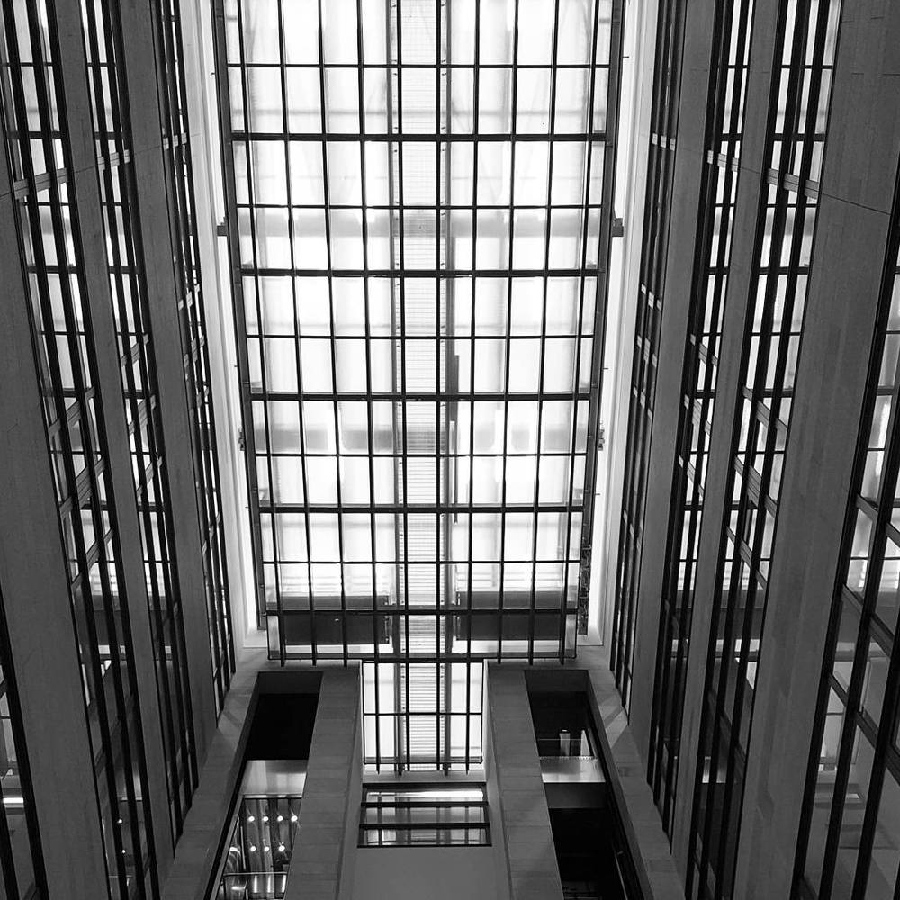 A black-and-white photo of a tall glass-and-steel atrium with a grid pattern of windows.