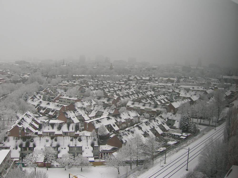 A hazy aerial view over snow-covered houses and gardens in Utrecht under an overcast sky.