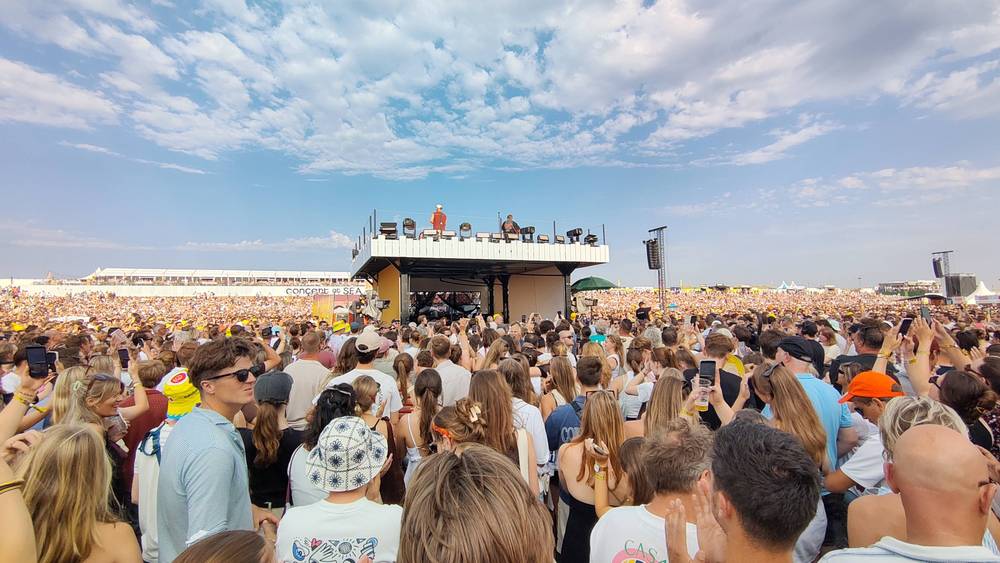 A large festival crowd faces a stage with performers.