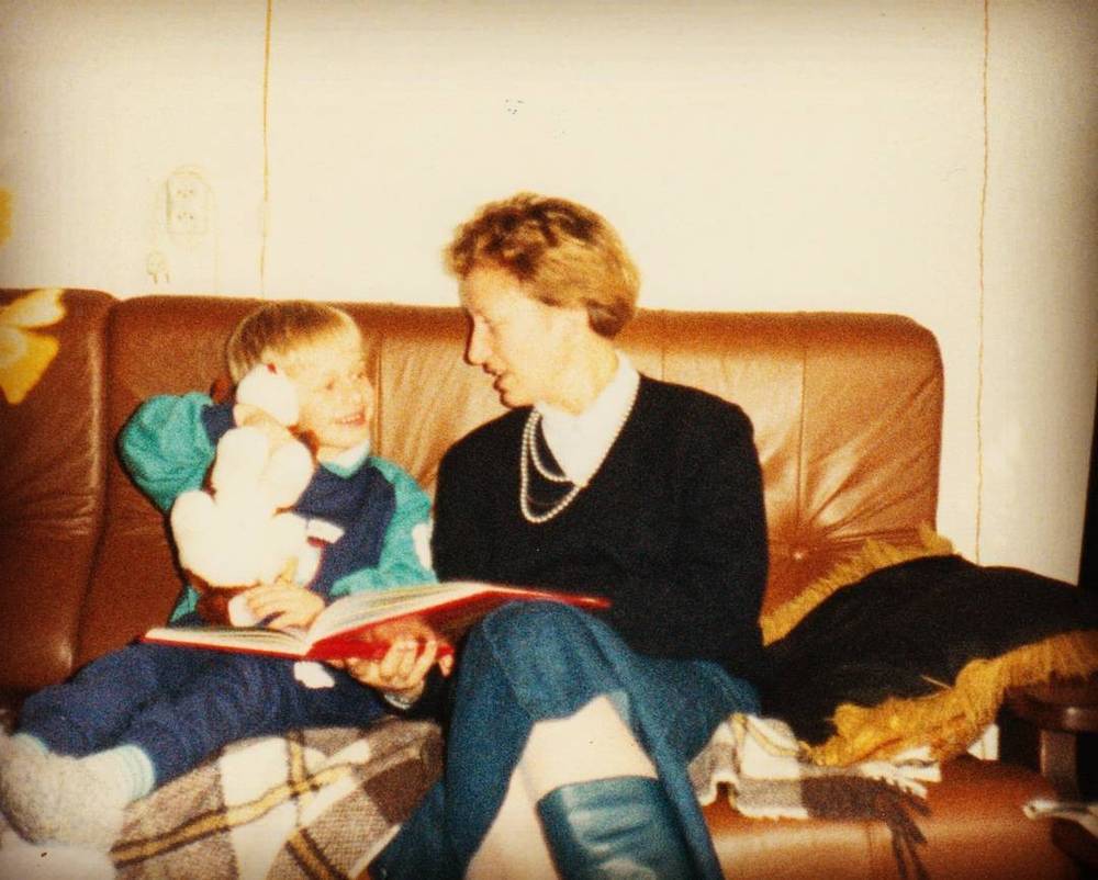 Vintage photo of a woman reading a book to a young child on a brown leather sofa.