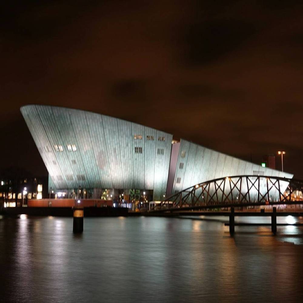 The NEMO Science Museum building beside an illuminated bridge at night.