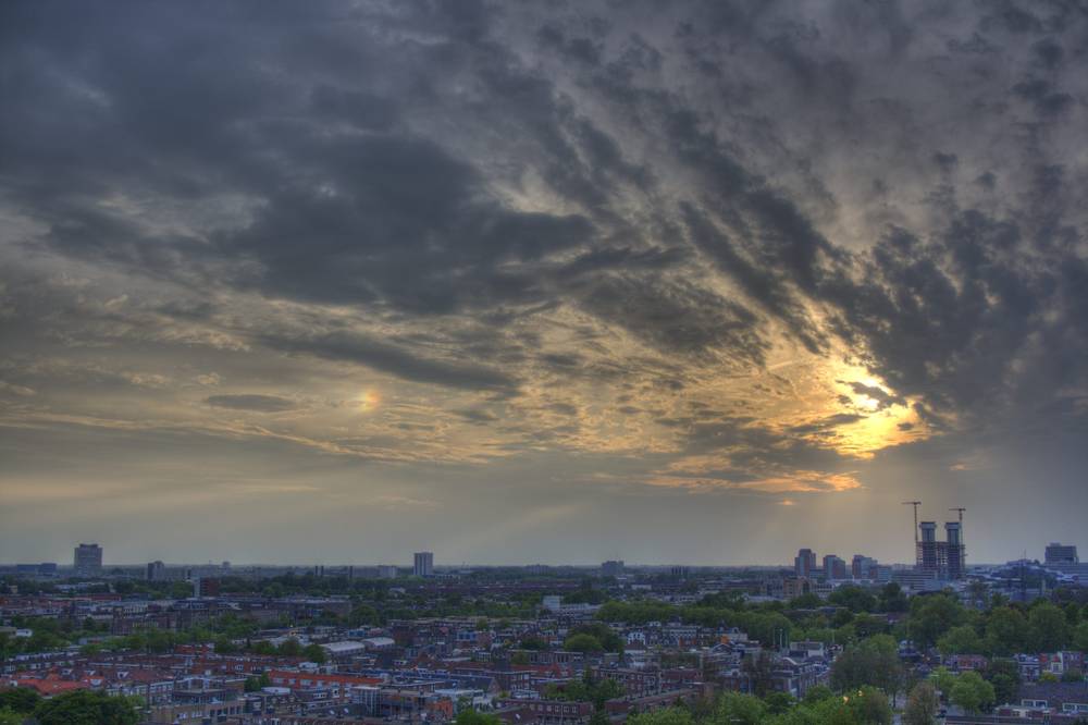 A colorful sun dog glowing beside the sun in streaked clouds above the Utrecht skyline.