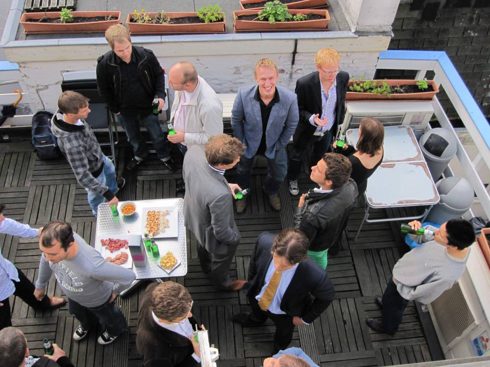 A group of colleagues chats over drinks and snacks on a rooftop terrace.
