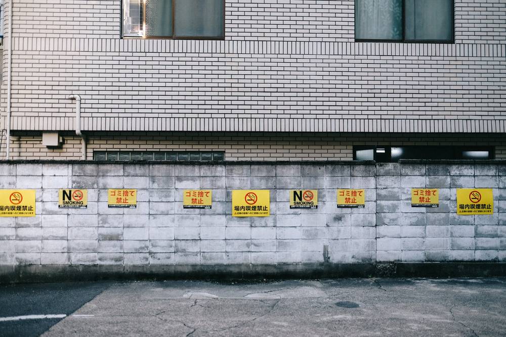 The same signs shown from straight on. The signs are two different sizes, the slightly smaller ones saying “ゴミ捨て禁止” and “NO SMOKING,” the larger ones saying “場内喫煙禁止”
