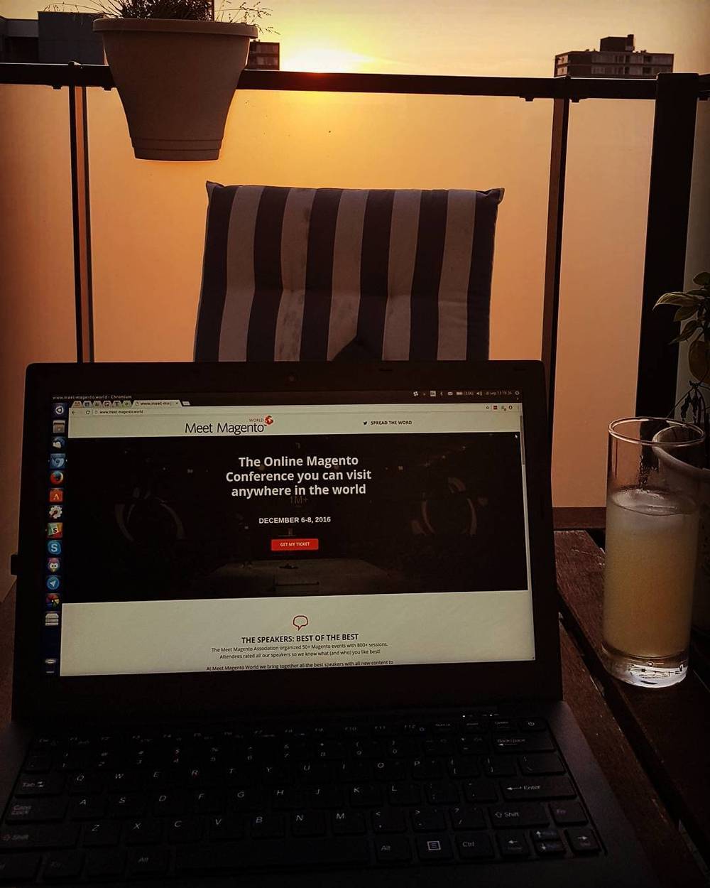 A laptop showing the Meet Magento conference website on a balcony table at dusk.